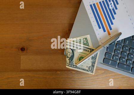 Dollar bills, a pen, and a laptop with a declining bar graph printed on paper symbolizing financial analysis, budget management, and investment planni Stock Photo