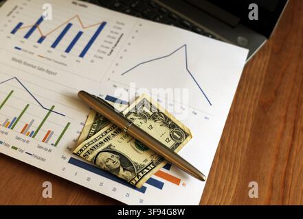 Business charts and graphs detailing revenue and sales data, featuring a dollar bill and a pen, representing financial planning, investment, and marke Stock Photo