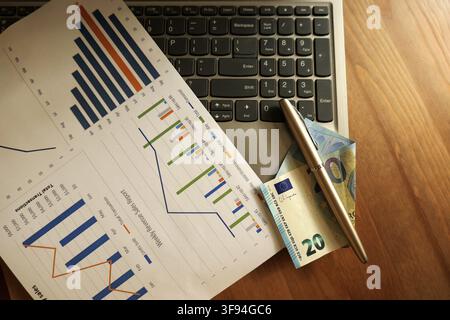 Overhead view showing a business professional analyzing financial performance data with charts and graphs, utilizing a laptop, pen, and euro currency Stock Photo