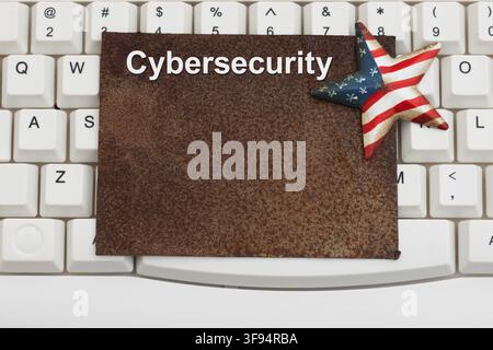 Cybersecurity text on a rusty sign with American flag star on a white computer keyboard for domestic cyber security vulnerabilities Stock Photo