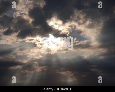 An atmospheric sunset with the sun illuminating the cloud cover and sending its rays through the sky. Stock Photo