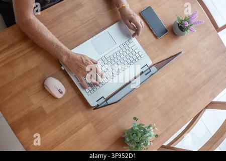 A top view of a person using a laptop touchpad at a wooden table. Remote freelance workspace, online home office business, modern lifestyle layout. Stock Photo