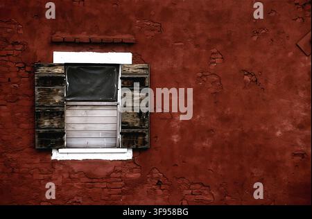 Vintage 35mm film photo of an old wooden window on a rustic red plaster wall with copy space and authentic film grain texture. Stock Photo
