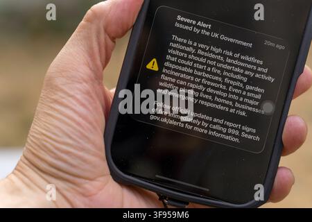 London, UK. 14th August 2026. A close-up of a hand holding a mobile phone displaying the UK Government's "Severe Alert" emergency warning of a very high national wildfire risk. The alert, sent to phones across England and Wales on 14 August 2026, followed a series of major wildfires including one in Stourbridge, West Midlands, that destroyed 19 homes, and marked the most extensive use of the UK's emergency alert system to date. Credit:xiu bao/Alamy Live News Stock Photo