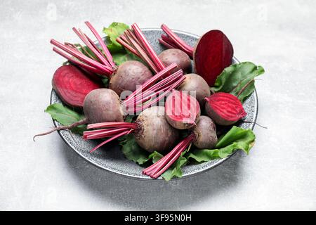 Whole and cut young beets with green leaves on gray textured table, closeup Stock Photo
