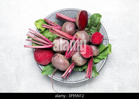Whole and cut young beets with green leaves on gray textured table, top view Stock Photo