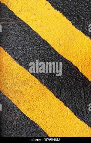 Abstract close-up of yellow and black hazard warning stripes painted on rough asphalt texture. Stock Photo