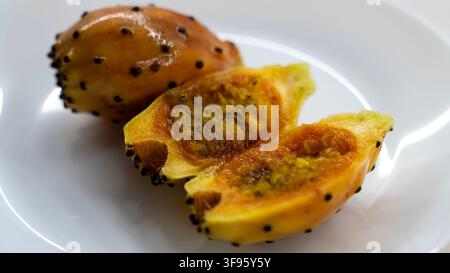 Ripe yellow dragon fruit cut in half on a white plate, showing juicy golden flesh with small black seeds and textured yellow skin. Stock Photo