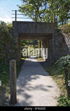 Stone and concrete former railway bridge crossing above a concrete pedestrian path at Nant Y Pandy Nature Reserve, Anglesey, North Wales, UK Stock Photo