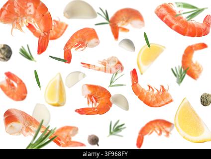 Boiled shrimps, lemon wedges, garlic cloves and spices falling on white background Stock Photo