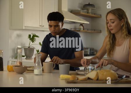 Diverse couple preparing breakfast at kitchen island, spreading butter on sliced bread Stock Photo