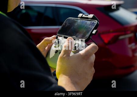 Drone pilot holding remote controller with connected mobile device displaying flight interface representing aerial surveying and control Stock Photo