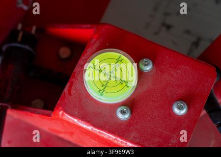 Circular bullseye spirit level gauge mounted on red industrial machinery frame for precise angle measurement and surface leveling control Stock Photo