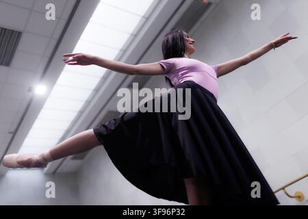 Ballet dancer practices in a studio with large windows and bright lighting during daytime Stock Photo