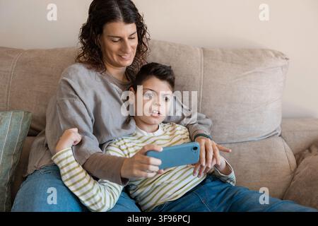 Mother and son relaxing on sofa using smartphone Stock Photo