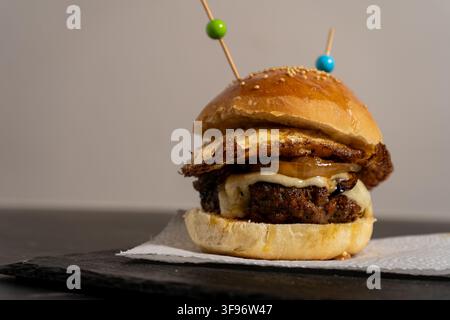 Mouth-watering gourmet burger with egg and cheese on a toasted brioche bun. The sandwich sits on a white paper towel over a dark stone surface, highli Stock Photo