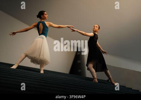 Two ballet dancers performing an elegant partnered pose on a modern staircase during rehearsal under soft architectural lighting Stock Photo