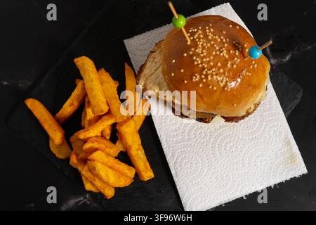 Delicious hamburger with two beef patties, fried egg, melted cheese and caramelized onions, served with French fries and ketchup. Stock Photo