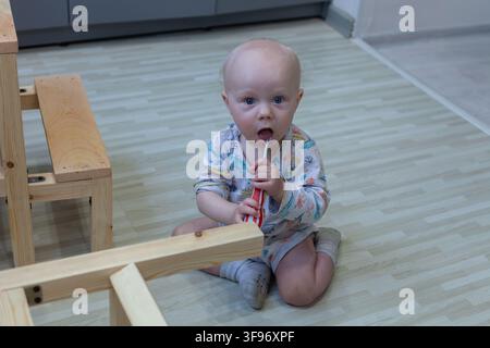 Baby sitting with a tool beside a wooden helper tower Stock Photo
