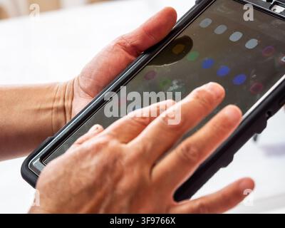 Close-up photograph of hands interacting with a tablet displaying a colorful digital interface. The image represents modern technology, digital intera Stock Photo
