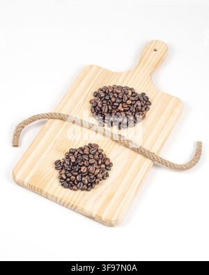 Overhead view of two piles of roasted coffee beans on a light wooden board, divided by a curved jute rope against a clean white background. Stock Photo