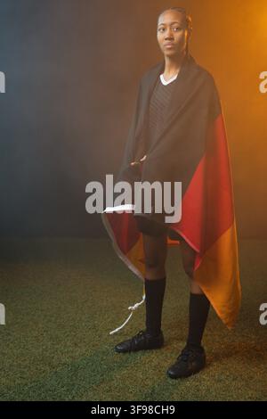 African American female standing on artificial turf in studio, wearing black jersey, cleats, wrap Stock Photo