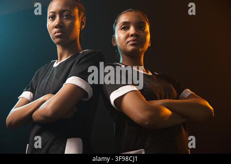 Two African female athletes standing in studio with arms crossed, wearing matching black jerseys Stock Photo