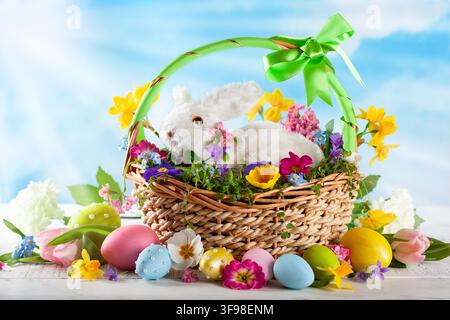 Easter composition with little white bunny in basket, spring flowers and colorful Easter eggs . Easter Card with copy space. - Photomontage Stock Photo