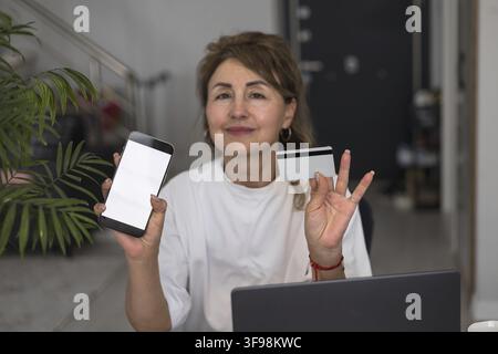 Mature pretty woman using credit card for online payment at home. Successful middle aged woman doing online shopping using laptop. Closeup female hand Stock Photo