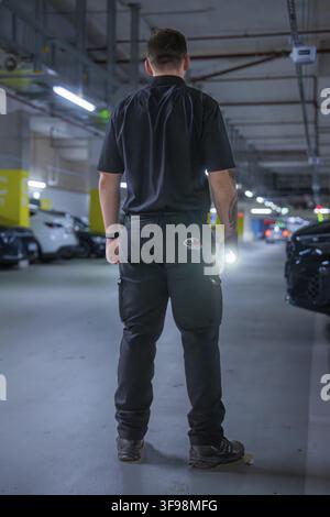 Security guard standing in an illuminated parking garage wearing black uniform with flashlight, Milaneo, Stuttgart, Germany Stock Photo