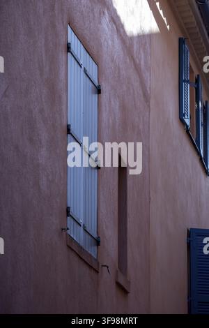 Closed pale blue-gray shutters line a pink stucco wall viewed at an angle, Saint-Tropez, Var, Provence-Alpes-Cote d'Azur, France Stock Photo