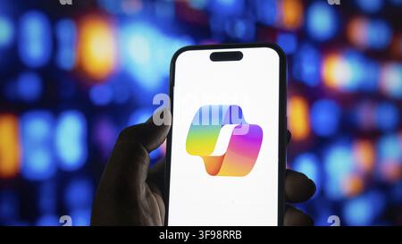 Microsoft copilot mobile application icon shown on modern cell phone against bokeh light background. Hand holding mobile device with colorful ai assis Stock Photo