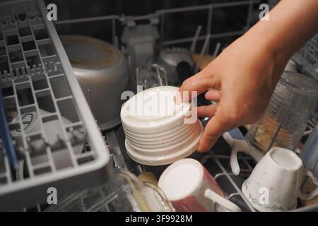 Hand places a dish in the dishwasher during clean up Stock Photo