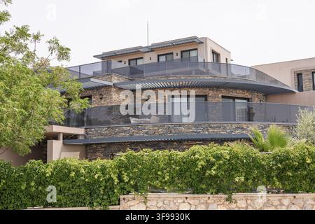 Modern stone house with large windows and balconies in Bodrum, Turkiye. Surrounded by greenery and a stone wall, showcasing contemporary architecture Stock Photo