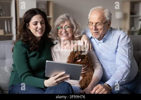 Granddaughter spend leisure with grandparents watching content on digital tablet Stock Photo