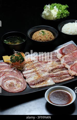 Japanese yakiniku set with assorted raw meats, rice, soup, salad, and dipping sauce on a black table. Stock Photo