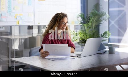 Businesswoman reviewing documents at workplace desk with laptop Stock Photo