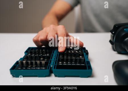 Close-up of handyman selecting bit from comprehensive driver bit set, preparing to use cordless electric power drill for upcoming diy project or home Stock Photo