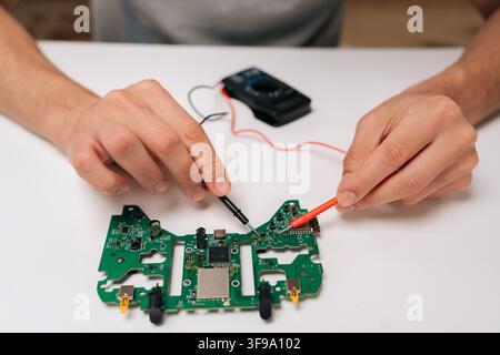 Repairman hands troubleshooting game controller circuit board with multimeter, checking electronic components and diagnosing potential issues during Stock Photo