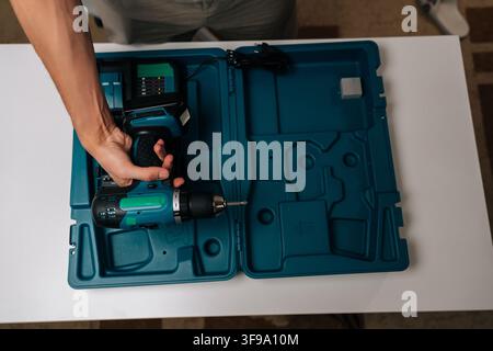High-angle view of foreman organizing powerful cordless drill with battery charger, screwdriver and drill bits neatly arranged in sturdy carrying case Stock Photo