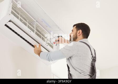Skilled male mechanic or repairman repairing conditioner at client house on white wall Stock Photo