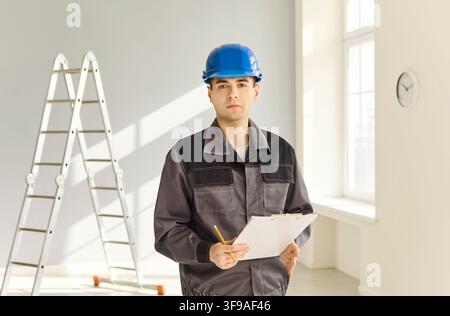 Contractor in blue hard hat with clipboard during indoor renovation inspection Stock Photo