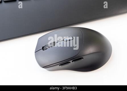 A black computer mouse rests on a clean white surface with a keyboard Stock Photo