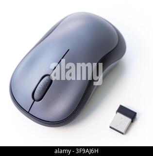 A gray wireless mouse and USB receiver are on a white surface Stock Photo