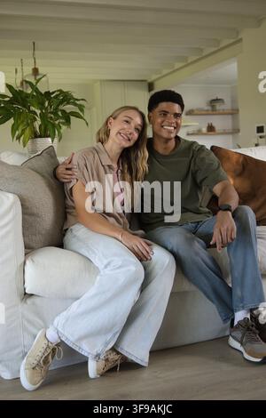Couple sitting closely on light-colored sofa in living room, showing wristwatch and sneakers. Pair, lounge, home, interior, cozy, neutral, warm Stock Photo