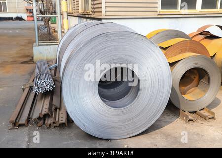 The image captures neatly stacked hot-rolled steel coils in an industrial storage environment. The metal surfaces exhibit a cool silvery-gray hue with Stock Photo