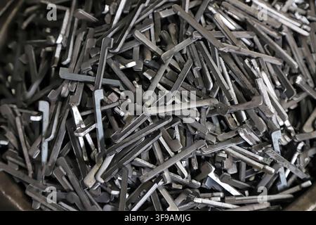 A large number of L-shaped metal stamped small parts are randomly piled up, showing the semi-finished state during the production process in the hardw Stock Photo