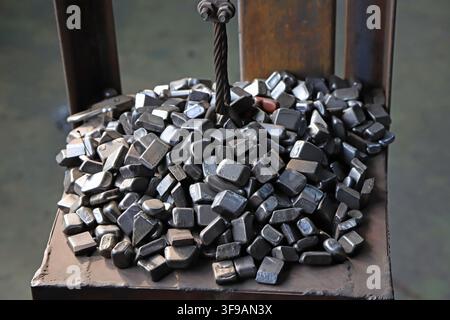 In an industrial production setting, a large number of square metal stamped small parts are piled on the platform, with a matte texture from metal pro Stock Photo