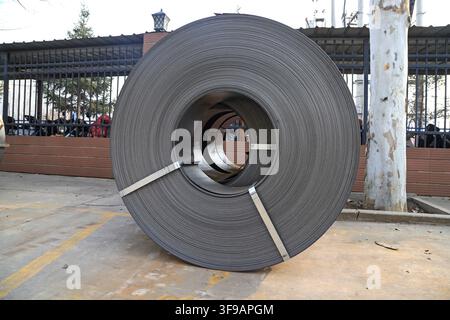 The image captures neatly stacked hot-rolled steel coils in an industrial storage environment. The metal surfaces exhibit a cool silvery-gray hue with Stock Photo