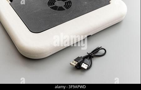 A white and black laptop cooling pad sits with a coiled USB cable Stock Photo